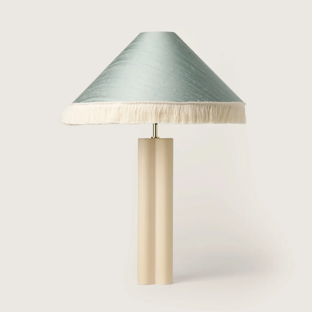 Elegant table lamp with a shade, white fringe, and a cream base.