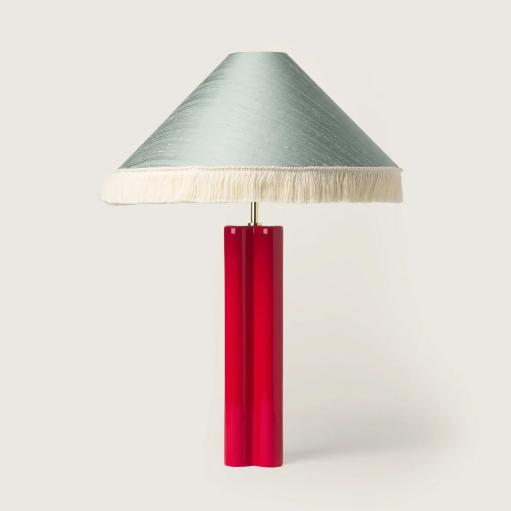 Elegant table lamp with a shade, white fringe, and a red base.