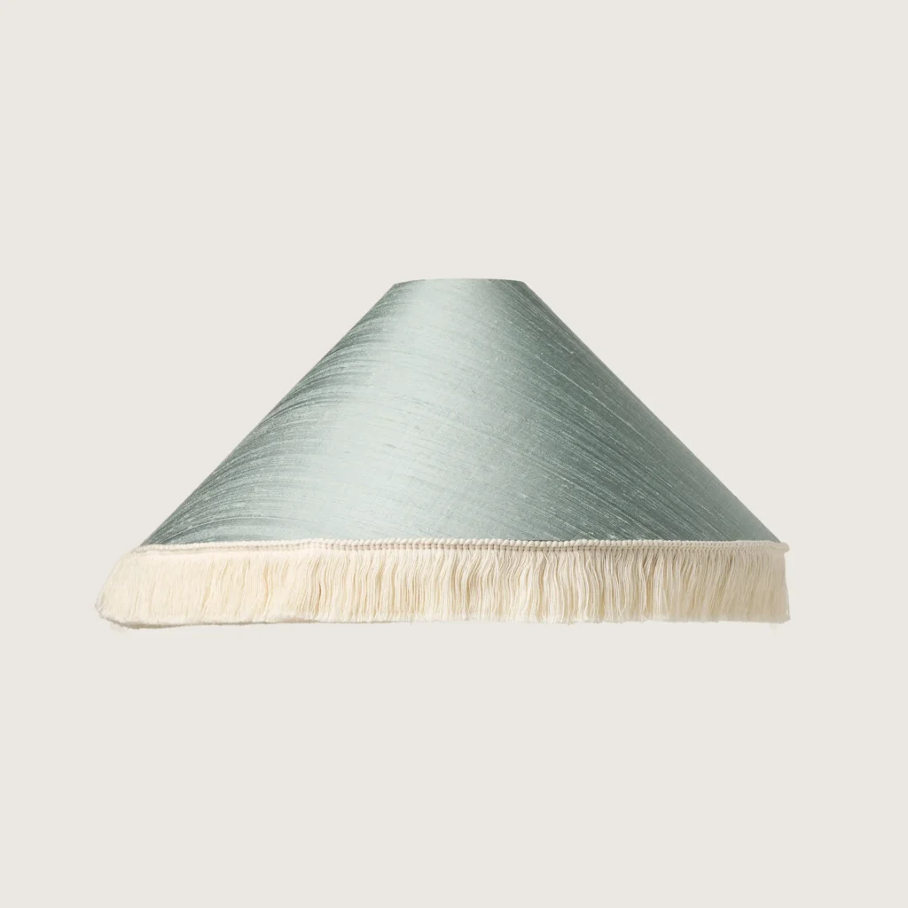 A beautifully formed conical lampshade, finished with a delicate white fringe along the bottom edge.
