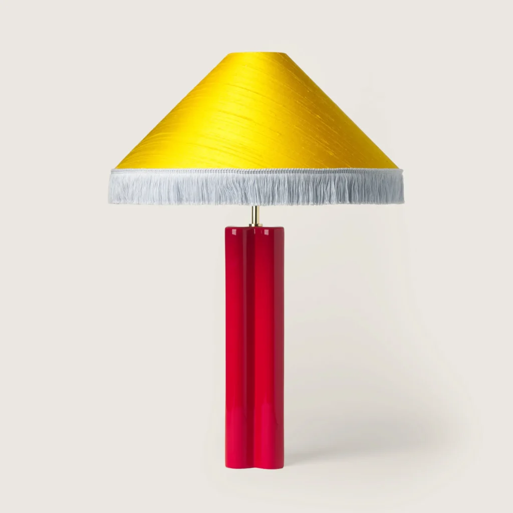 Elegant table lamp with a yellow shade, white fringe, and a red base.