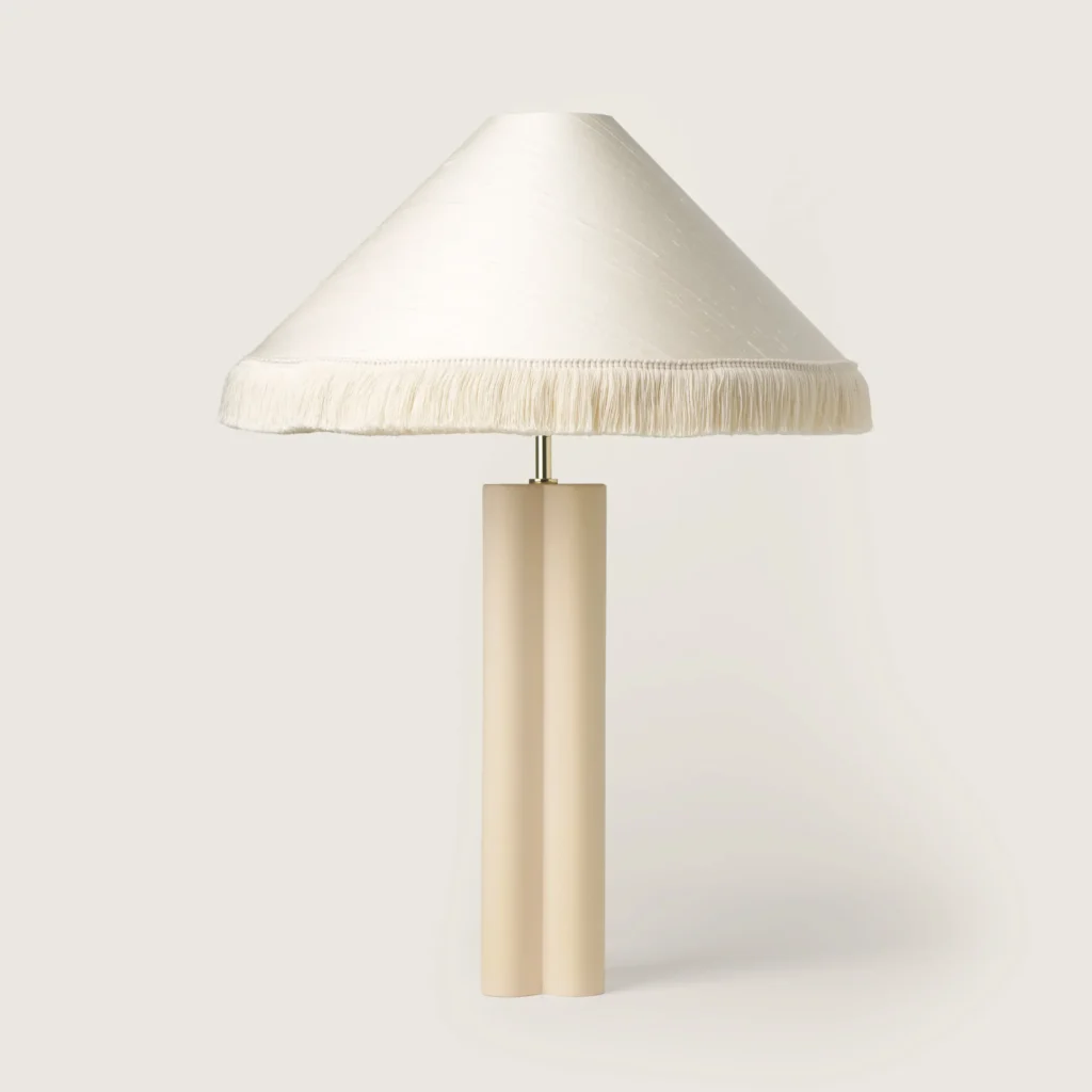 Elegant table lamp with a white shade, white fringe, and a cream base.