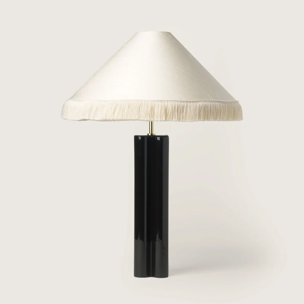 Elegant table lamp with a white shade, white fringe, and a black base.