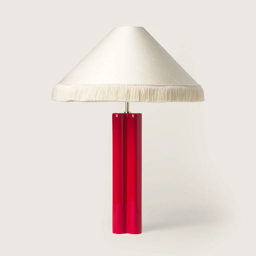 Elegant table lamp with a white shade, white fringe, and a red base.