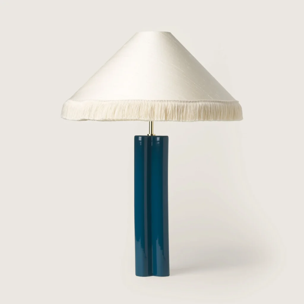 Elegant table lamp with a white shade, white fringe, and a blue base.