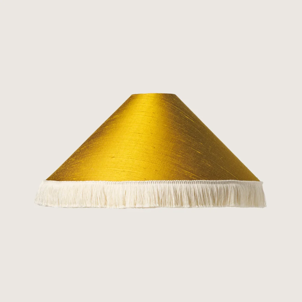 A beautifully formed yellow conical lampshade, finished with a delicate white fringe along the bottom edge.