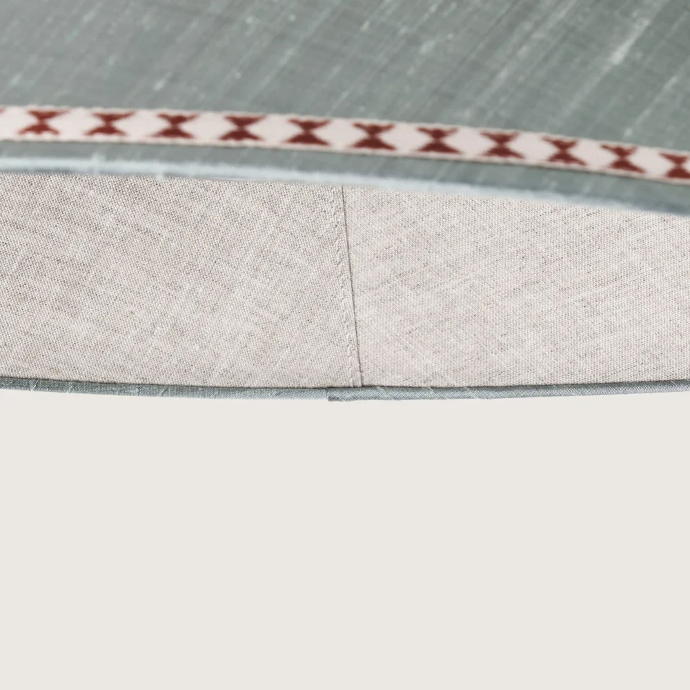 Close-up of a beautifully formed grey conical lampshade, decorated with a delicate geometric pattern along the top and bottom edges.