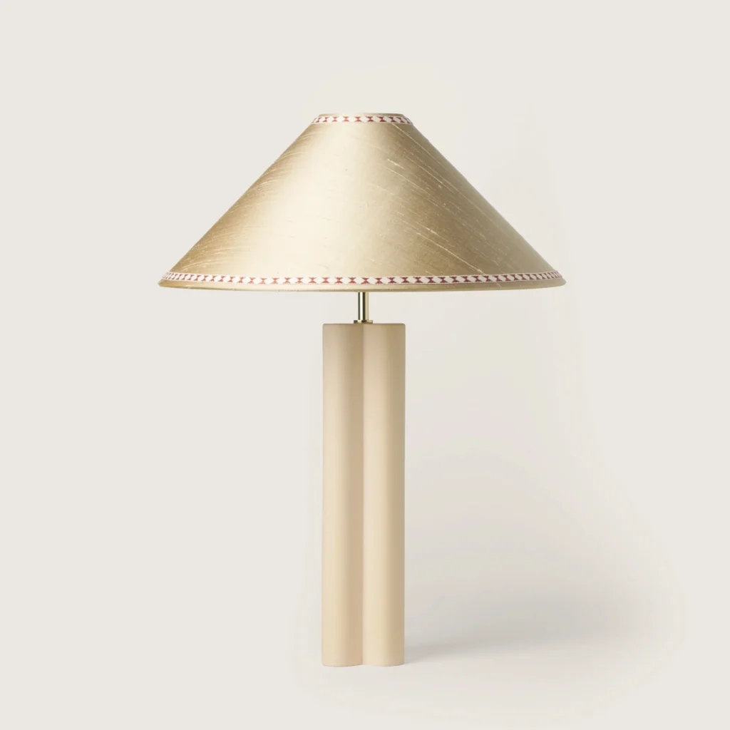 Elegant table lamp with a off-white shade, ribbon, and a cream base.