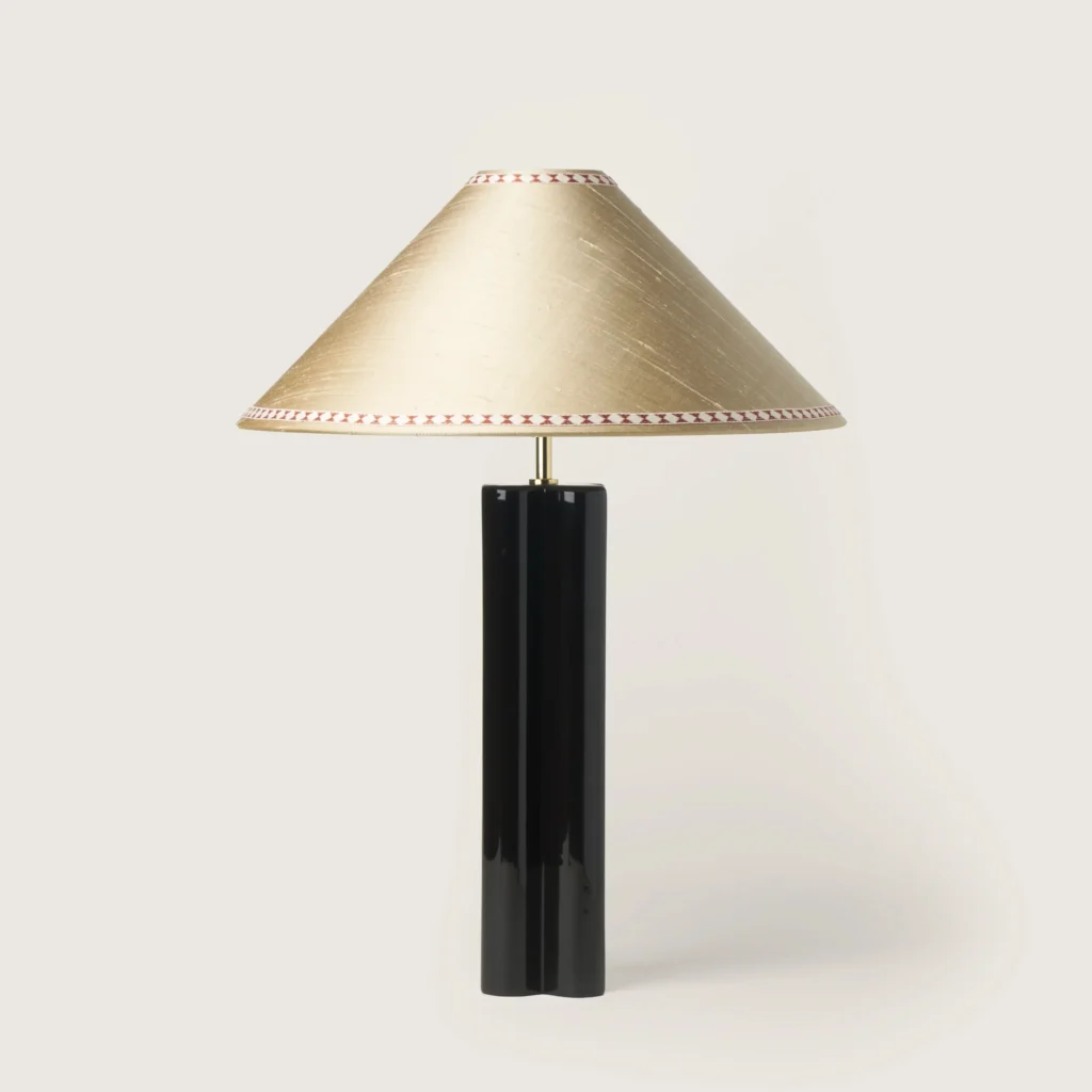 Elegant table lamp with a off-white shade, ribbon, and a black base.