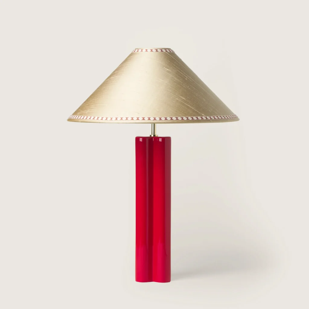 Elegant table lamp with a off-white shade, ribbon, and a red base.
