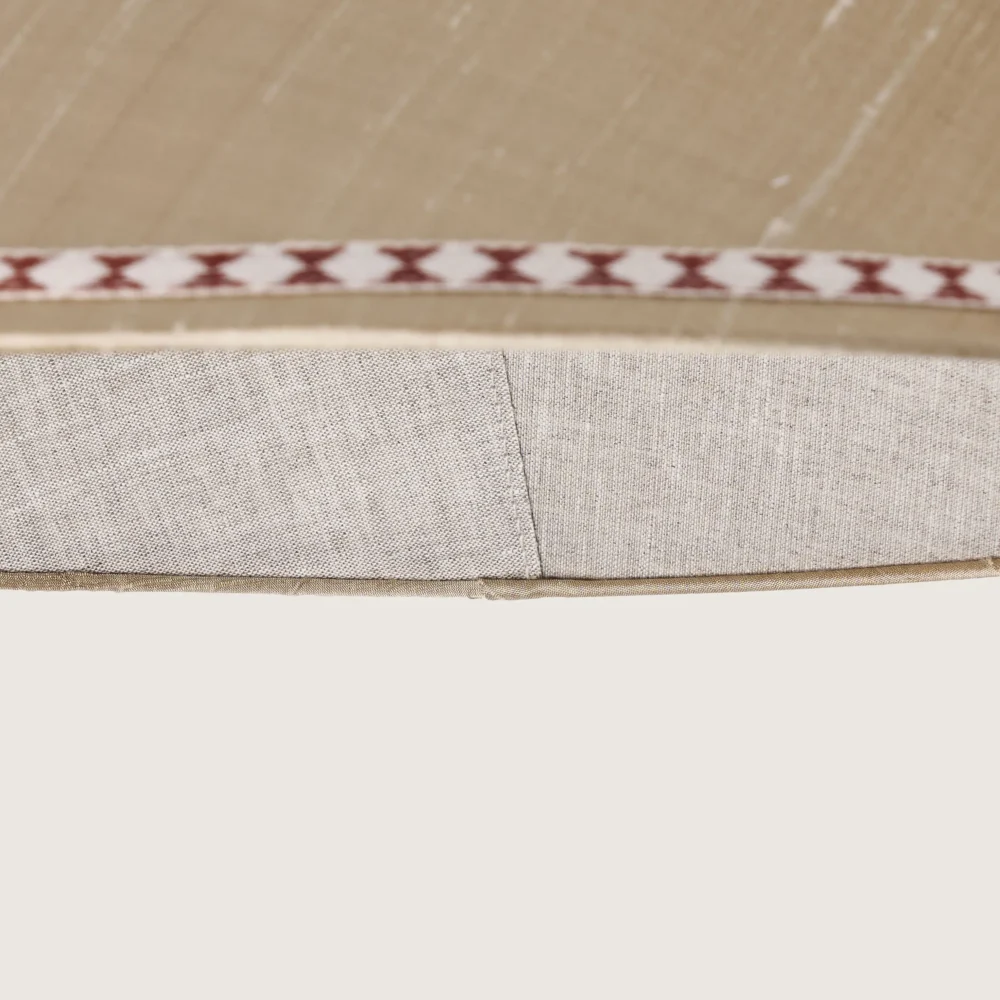 Close-up of a beautifully formed cream conical lampshade, decorated with a delicate geometric pattern along the top and bottom edges.