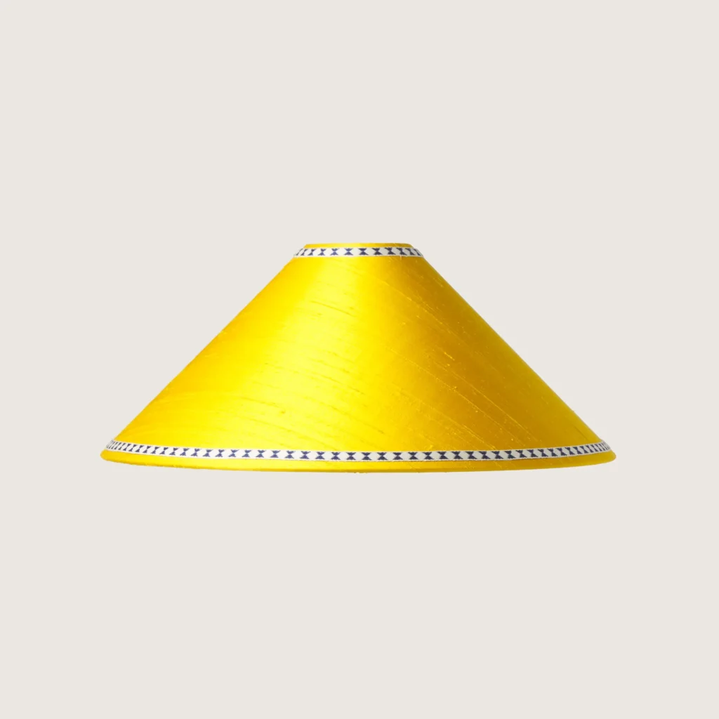A beautifully formed yellow conical lampshade, decorated with a delicate geometric pattern along the top and bottom edges.