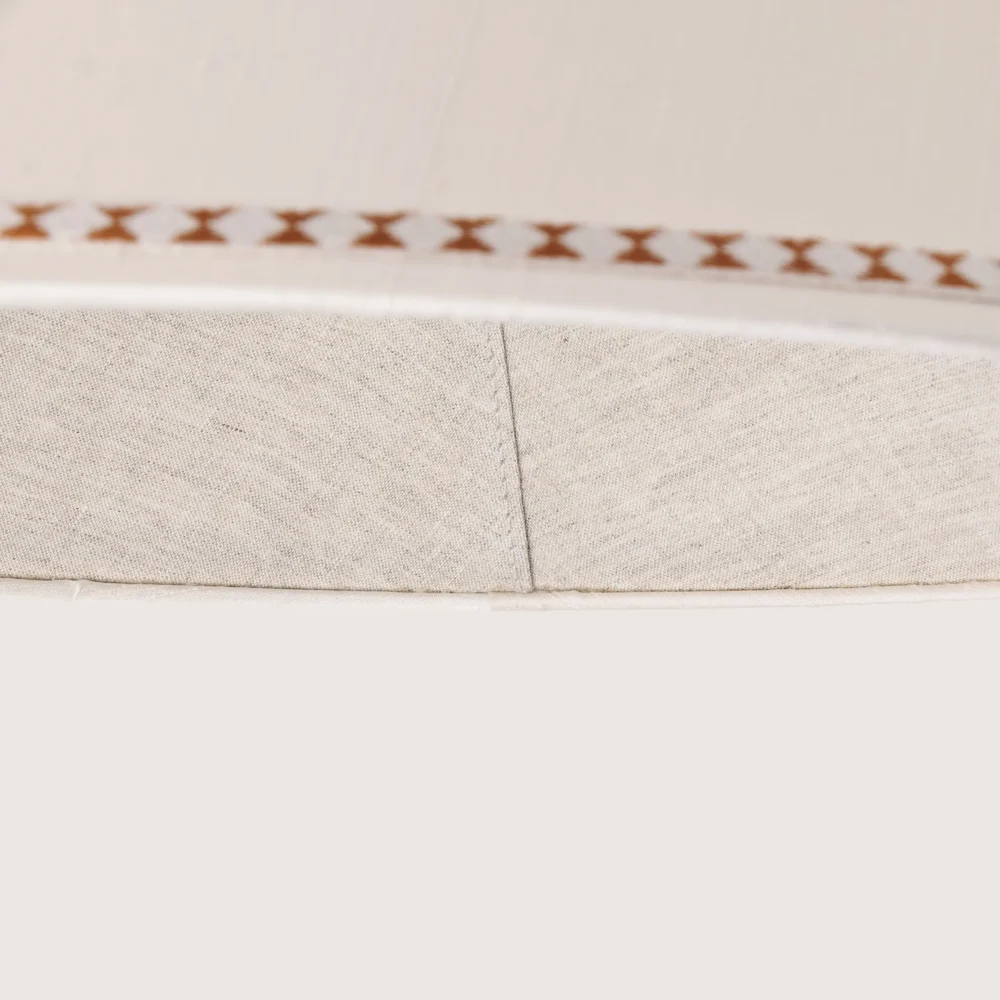 Close-up of a beautifully formed white conical lampshade, decorated with a delicate geometric pattern along the top and bottom edges.