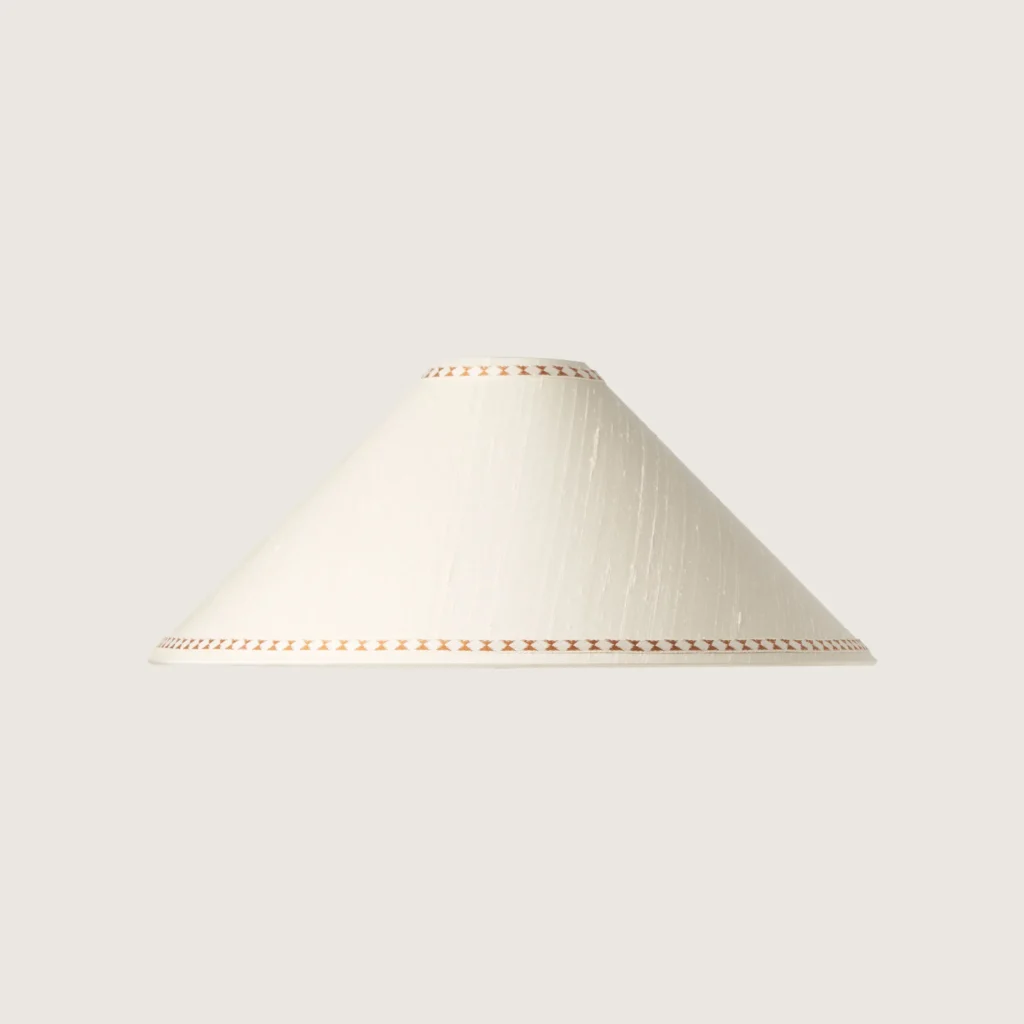A beautifully formed white conical lampshade, decorated with a delicate geometric pattern along the top and bottom edges.