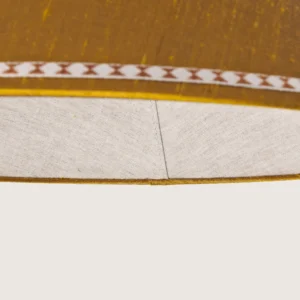 Tasiemki.kolor5-detal Close-up of a beautifully formed yellow conical lampshade, decorated with a delicate geometric pattern along the top and bottom edges.