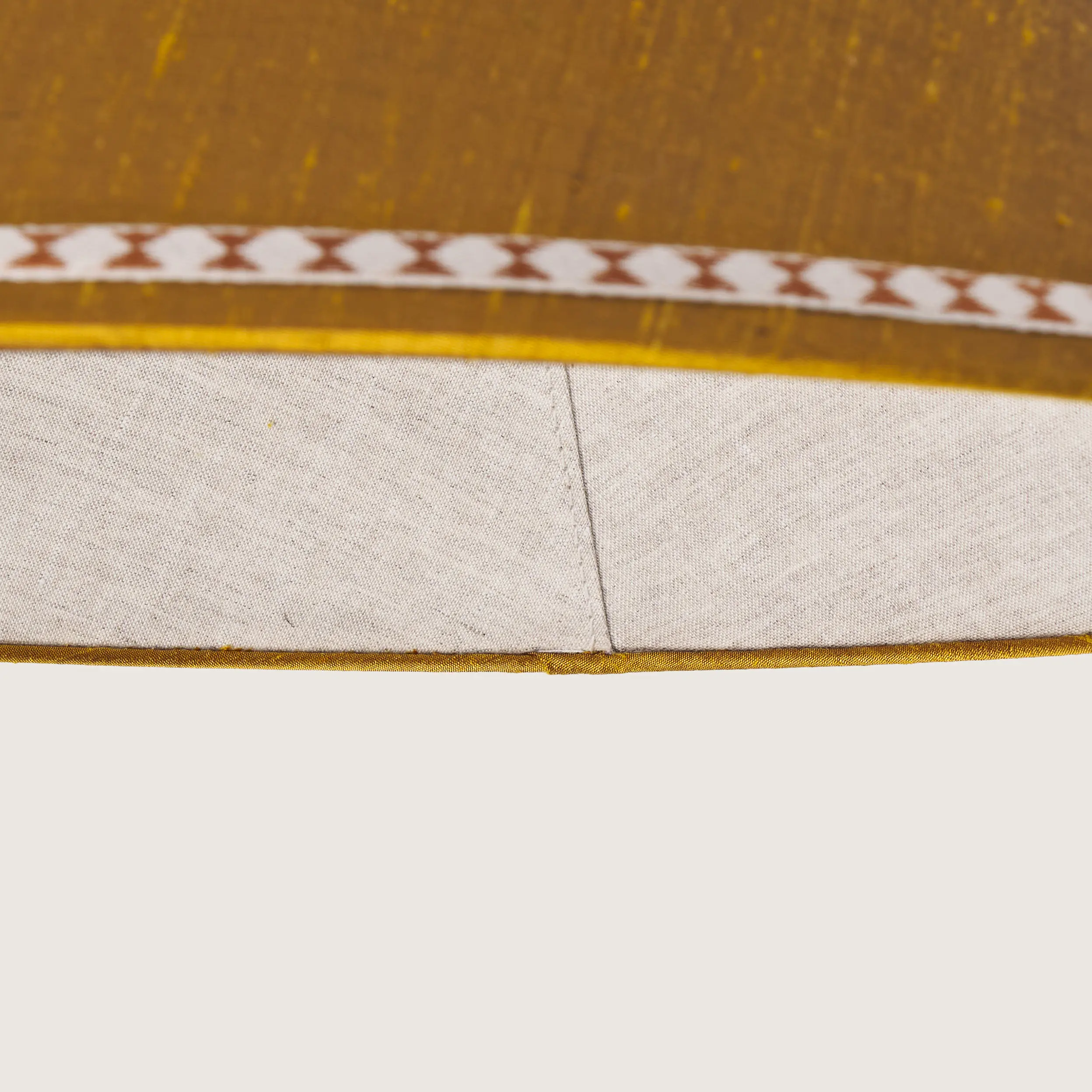 Tasiemki.kolor5-detal Close-up of a beautifully formed yellow conical lampshade, decorated with a delicate geometric pattern along the top and bottom edges.