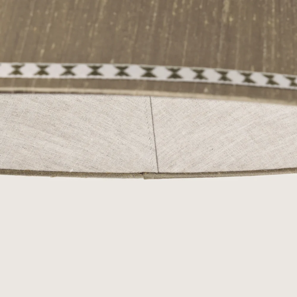 Close-up of a beautifully formed grey conical lampshade, decorated with a delicate geometric pattern along the top and bottom edges.